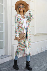 Woman in a tan fedora hat, sunglasses, and a long, multi-colored tweed-inspired knit cardigan with fringe detail, holding a clutch.