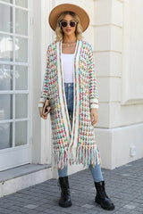 Woman in a tan fedora hat, sunglasses, and a long, multi-colored tweed-inspired knit cardigan with fringe detail, holding a clutch.