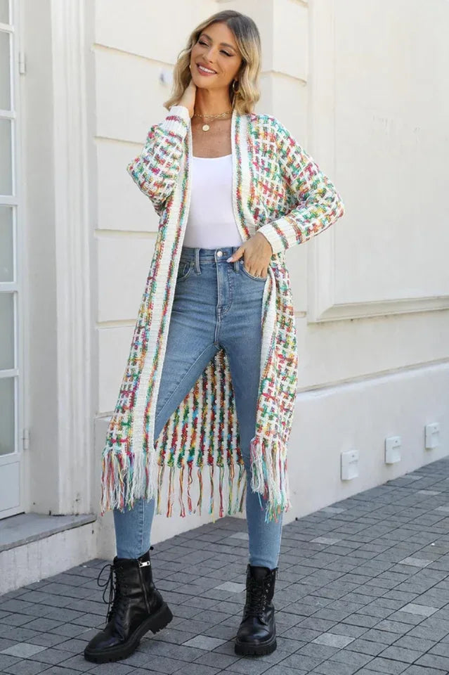 Woman wearing a long, multi-colored tweed-inspired knit cardigan with fringe detail, blue jeans, and black boots.