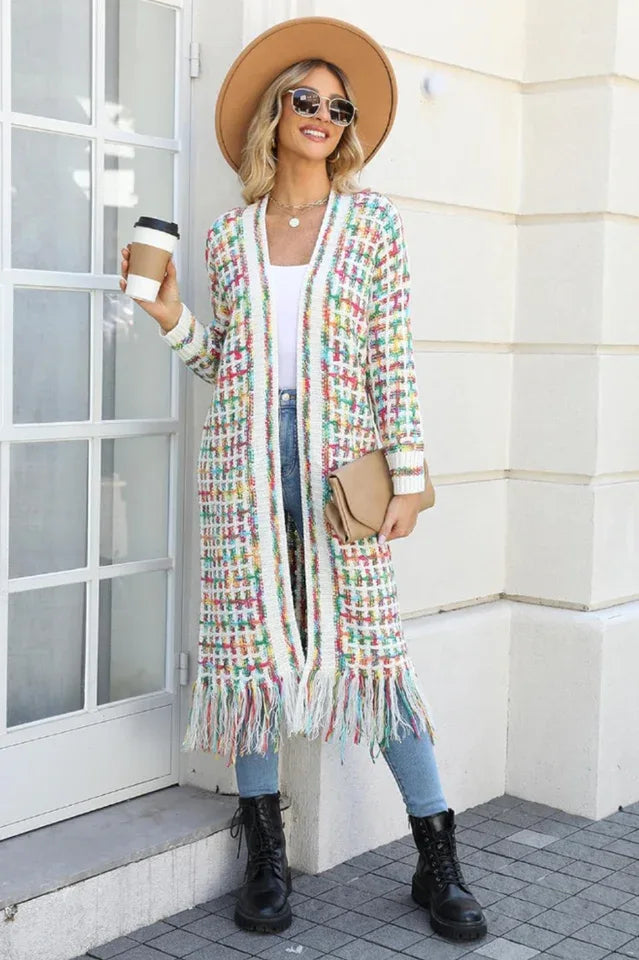 Woman in a tan fedora hat, sunglasses, and a long, multi-colored tweed-inspired knit cardigan with fringe detail, holding a coffee cup and a clutch.