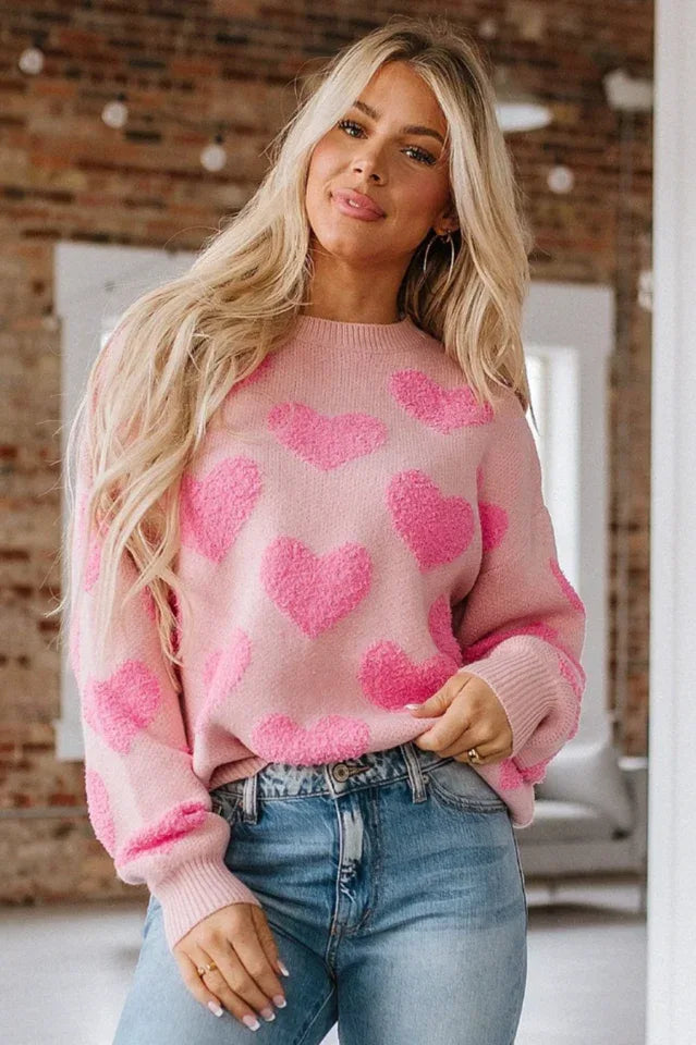 Woman wearing a pink crew neck sweater with a textured pink heart pattern and blue jeans.