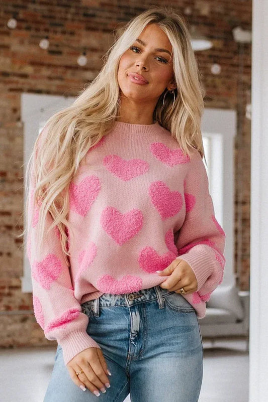 Woman wearing a pink crew neck sweater with a textured pink heart pattern and blue jeans.