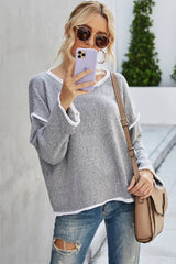 Woman in a grey textured knit sweater with white trim and distressed jeans, holding a smartphone and a crossbody bag.