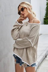 Woman in a beige textured knit sweater with white trim and denim shorts, posing with her arm across her chest.
