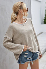 Woman in a beige textured knit sweater with white trim and denim shorts, with her hand in her pocket.