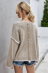 Back view of a woman wearing a beige textured knit sweater with white trim and denim shorts, showing fringe detail on the back.
