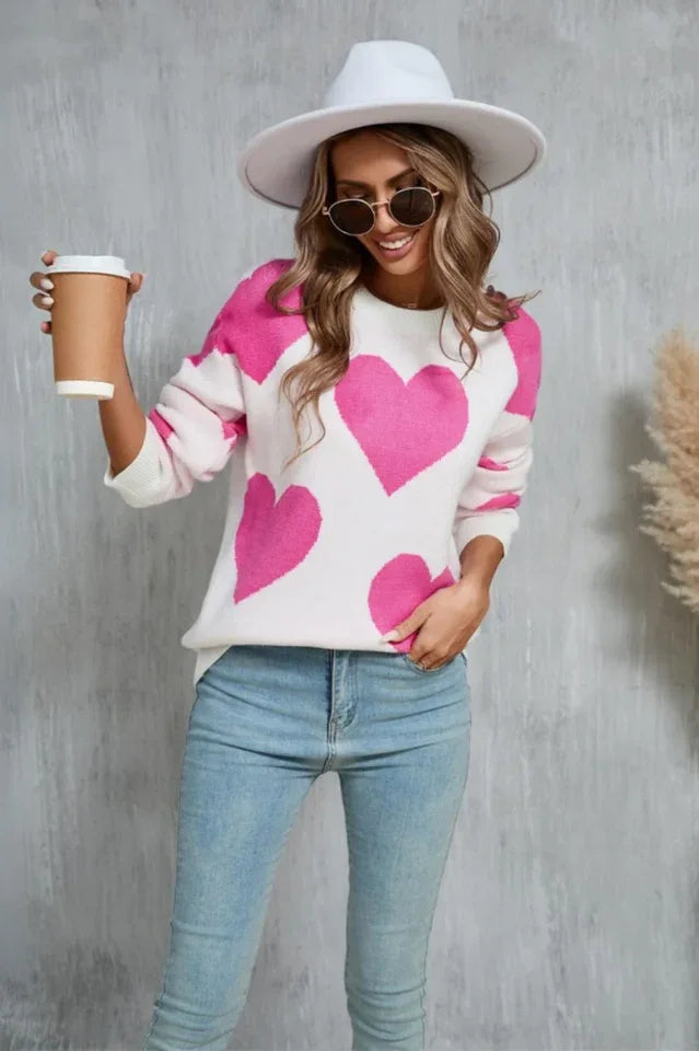 Woman wearing a white sweater with a pink heart print and holding a coffee cup.