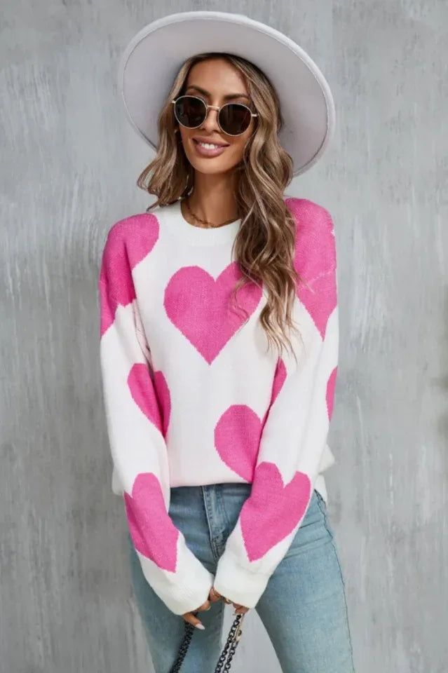 Woman wearing a white sweater with a pink heart print and a white hat.