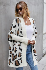 Woman wearing a white leopard print long cardigan over a white tank top and blue jeans.