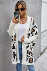 Woman taking a selfie while wearing a white leopard print long cardigan over a white tank top and blue jeans.