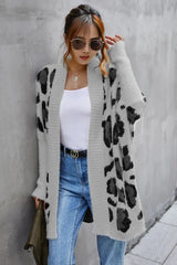 Woman wearing a grey leopard print long cardigan over a white tank top and blue jeans.