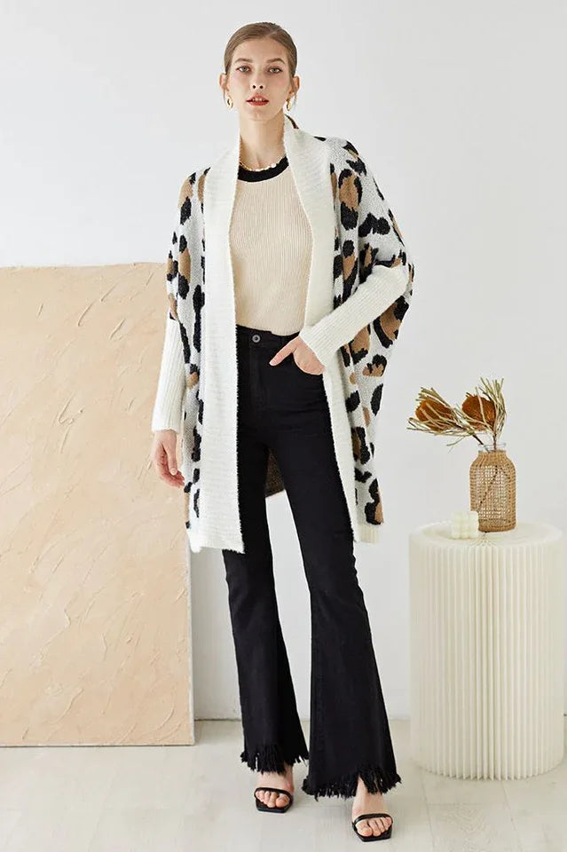 Woman wearing a cream long cardigan with a leopard print pattern over a cream top and black flared jeans.