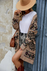 Woman in a tan geometric print long cardigan, white t-shirt, denim shorts, a wide-brimmed hat, and a brown crossbody bag
