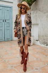 Woman wearing a tan geometric print long cardigan, white t-shirt, denim shorts, brown cowboy boots, and a wide-brimmed hat, standing outdoors