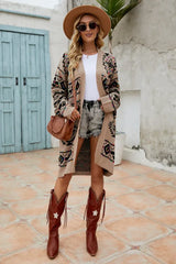 Full body shot of a woman in a tan geometric print long cardigan, white t-shirt, denim shorts, brown cowboy boots, and a wide-brimmed hat