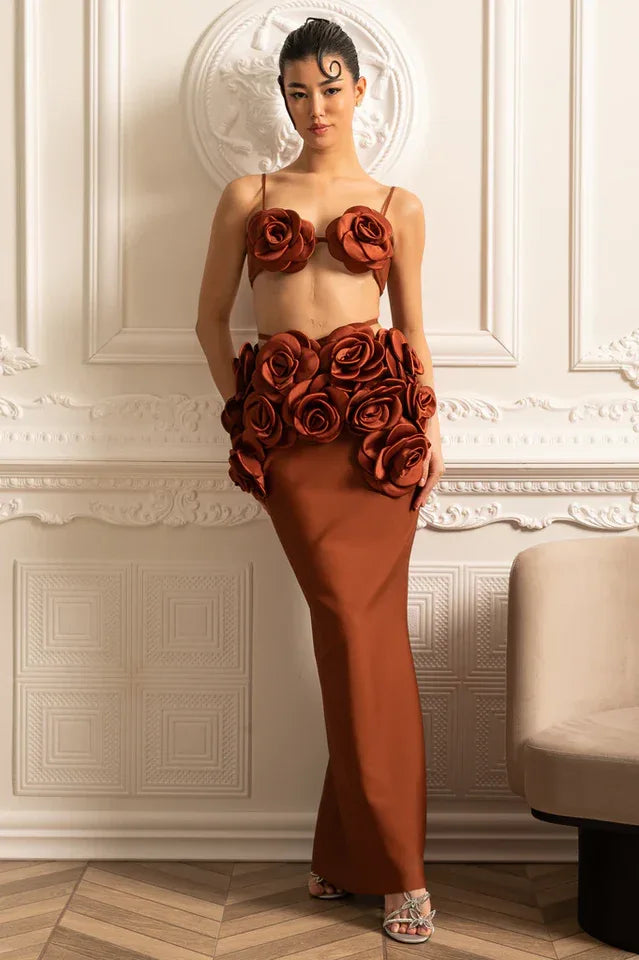 Woman wearing a rust-colored two-piece evening gown with rose embellishments on the bust and waist