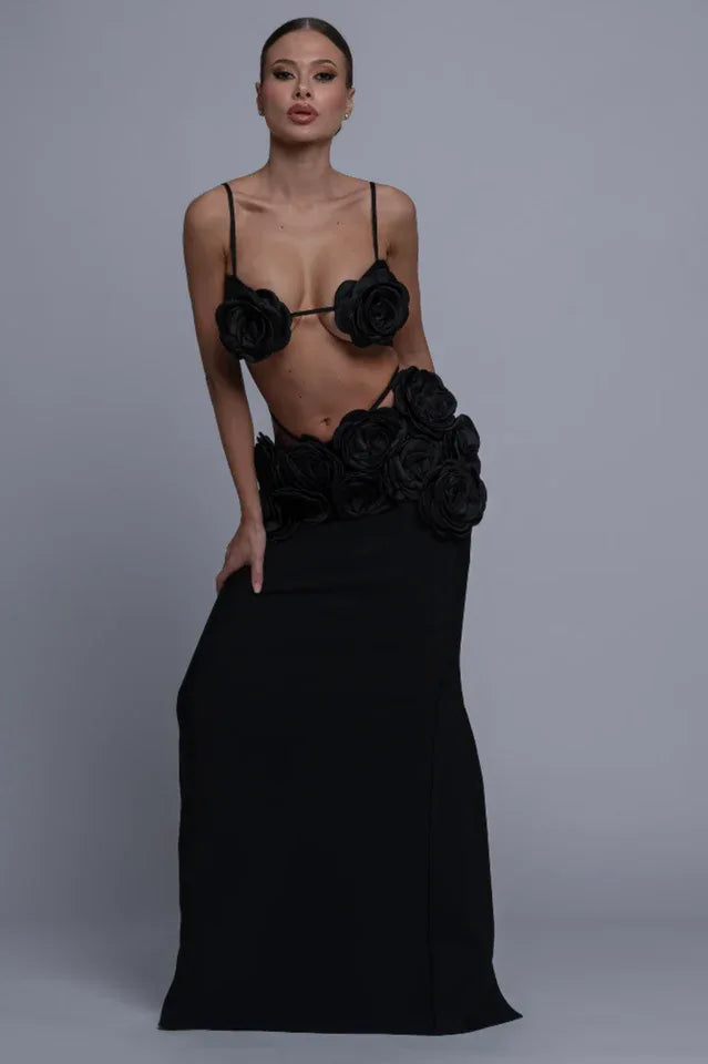 Woman posing in a black two-piece evening gown with rose embellishments, showcasing the cut-out waist