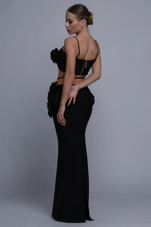 Back view of a woman in a black two-piece evening gown with rose embellishments, showing the zipper detail