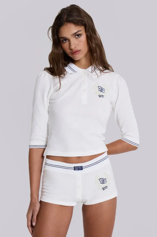 Model wearing a white cropped polo shirt with blue trim and matching white shorts with blue trim.