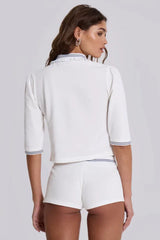 Back view of a model wearing a white cropped polo shirt with blue trim and matching white shorts with blue trim.