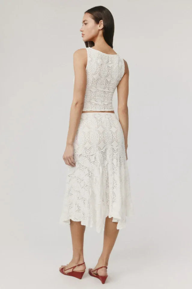 Back view of a woman wearing a white crochet knit cropped tank top and a white crochet knit asymmetrical hem midi skirt.