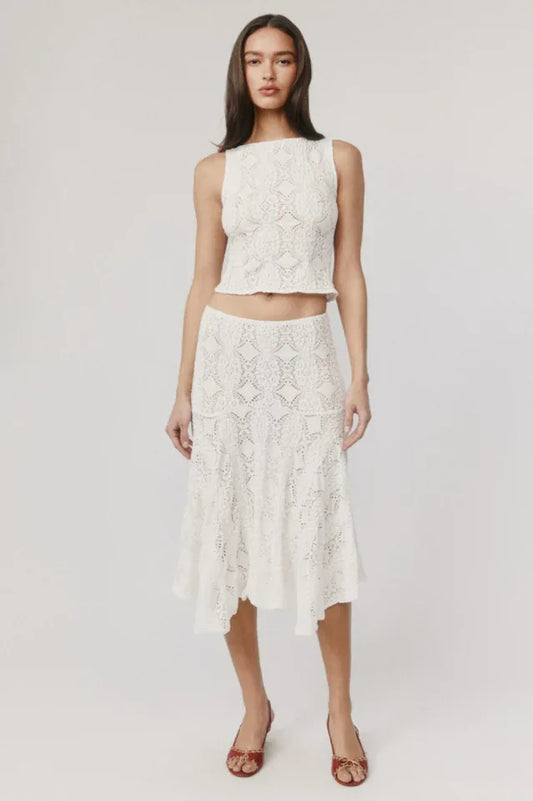Woman wearing a white crochet knit cropped tank top and a white crochet knit asymmetrical hem midi skirt.