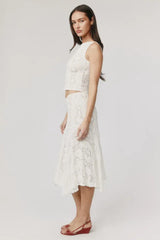 Side view of a woman wearing a white crochet knit cropped tank top and a white crochet knit asymmetrical hem midi skirt.