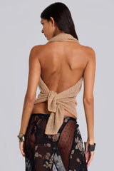 Woman wearing a gold halter knit top tied at the back, showcasing her back, paired with a black floral lace skirt.