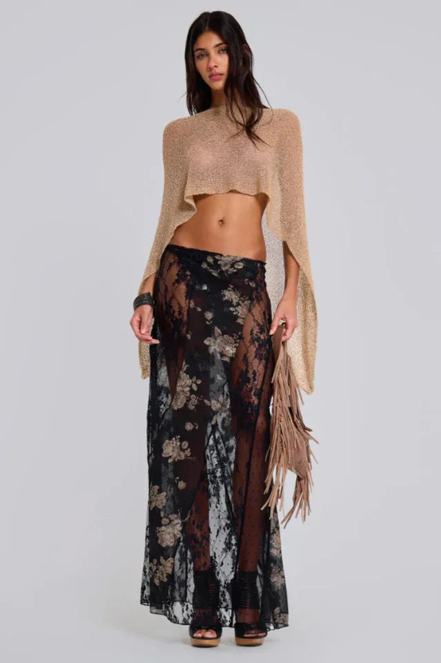 Woman wearing a gold cropped metallic knit poncho over a black floral lace skirt and black heels, front view.