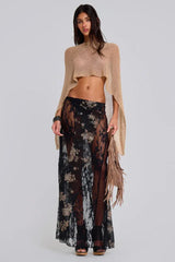 Woman wearing a gold cropped metallic knit poncho over a black floral lace skirt and black heels, front view.