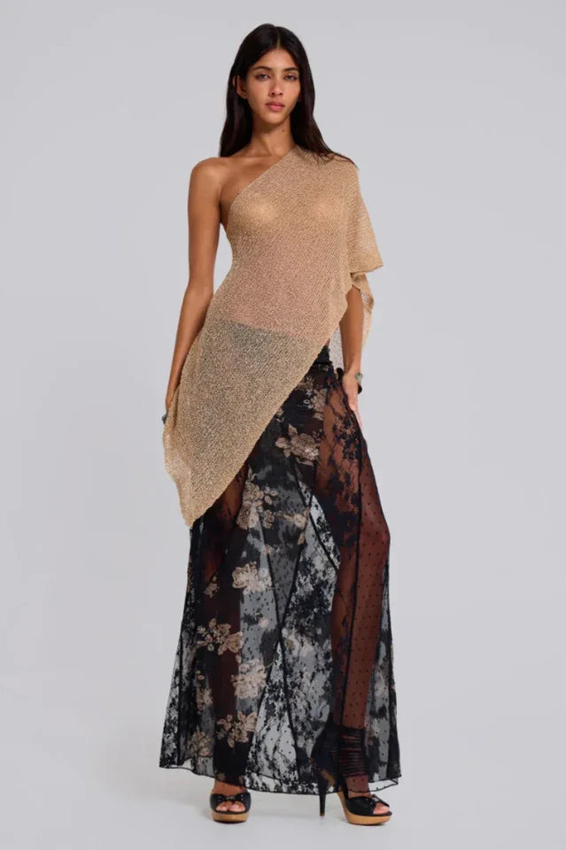 Woman wearing a gold asymmetrical one-shoulder metallic knit top draped over a black floral lace skirt, front view.