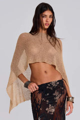 Woman wearing a gold cropped metallic knit poncho, revealing her midriff, paired with a black floral lace skirt, front view.