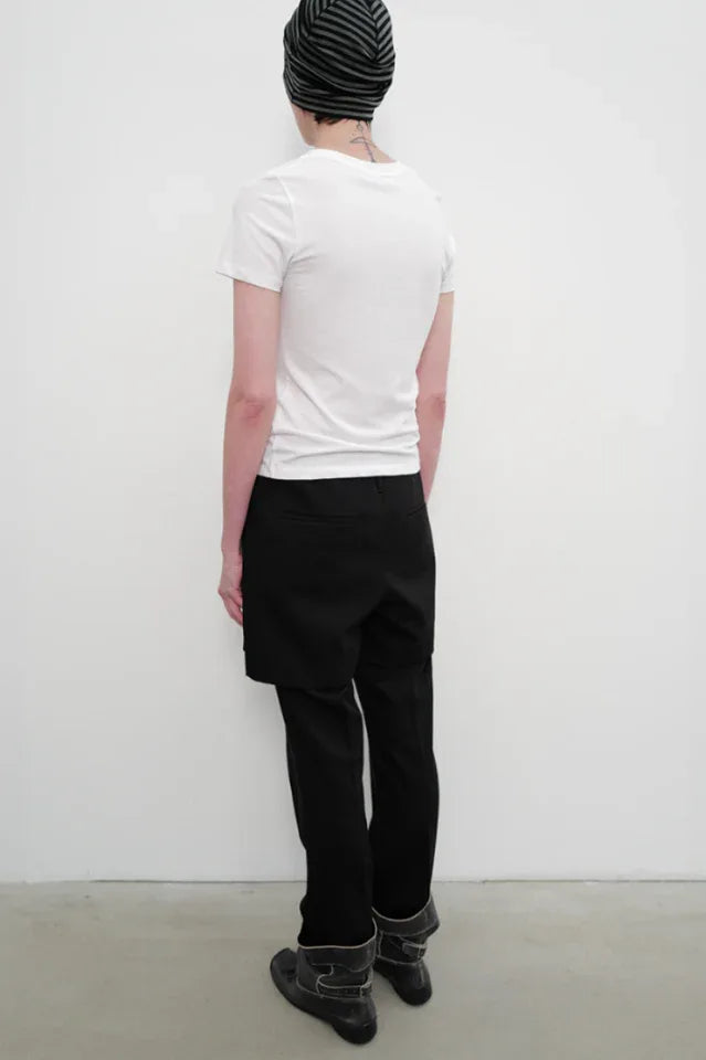 Back view of a model wearing a white crew neck t-shirt with a black and white graphic print on the chest, black shorts over black pants, and black boots.