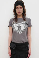 Model wearing a grey crew neck t-shirt with a black and white graphic print on the chest, a black belt bag, and a black pleated skirt.