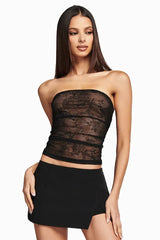 Woman wearing a black strapless lace tube top and a black mini skirt, front view.