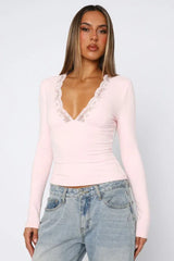Woman wearing a pink long-sleeved top with lace trim and blue jeans, front view