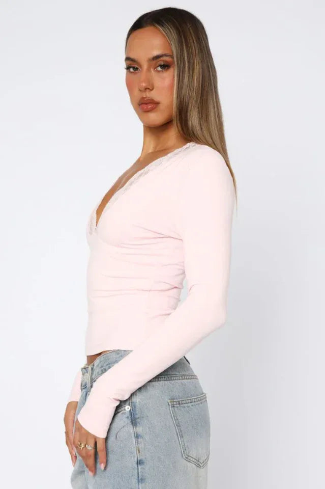 Woman wearing a pink long-sleeved top with lace trim and blue jeans, side view