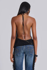 Back view of a model wearing a black halter top with an open back and studded trim, paired with blue jeans with fringe detailing.