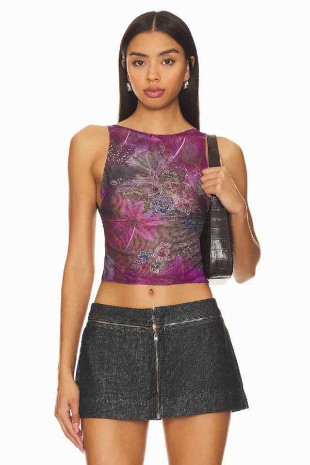 Woman wearing a purple sheer floral print sleeveless top with a black denim mini skirt and a black shoulder bag.