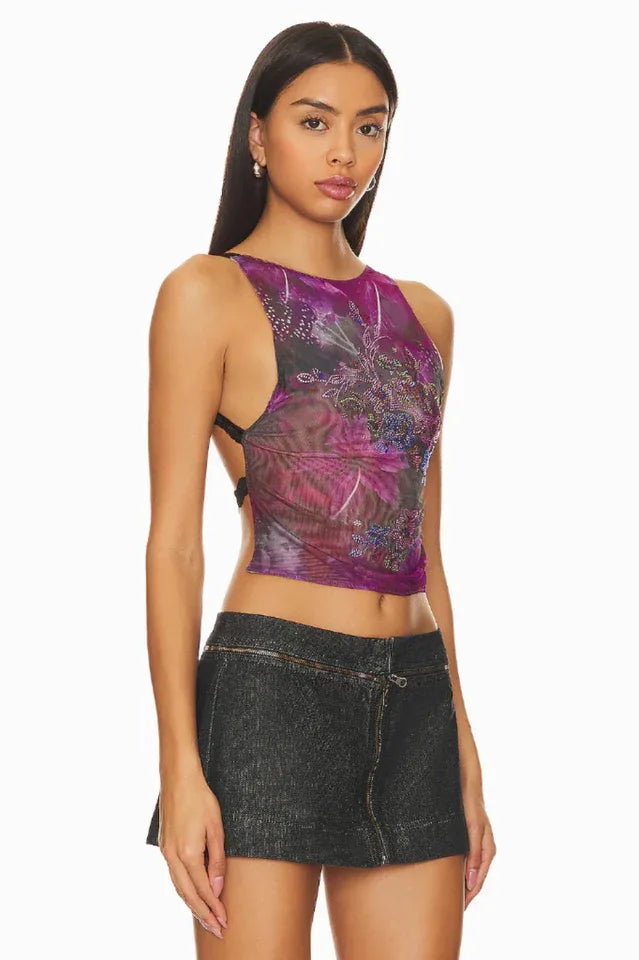 Side view of a woman wearing a purple sheer floral print sleeveless top with a black denim mini skirt.