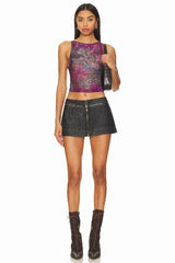 Full-length front view of a woman wearing a purple sheer floral print sleeveless top, black denim mini skirt, and dark brown lace-up boots.