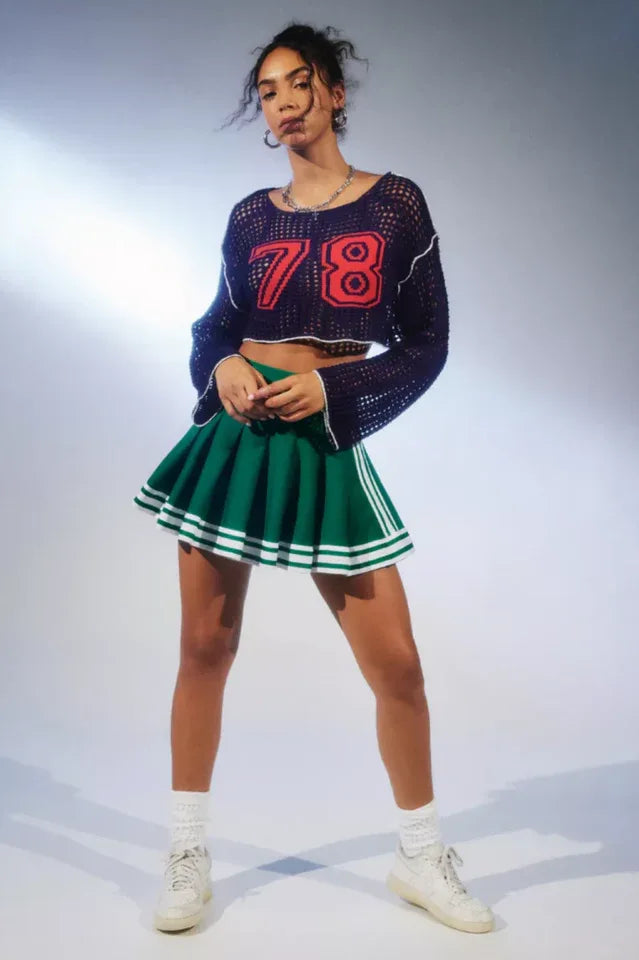 Close-up of a woman wearing a navy blue cropped open-knit sweater with red appliquéd numbers and white trim.
