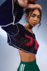 Woman wearing a navy blue cropped open-knit sweater with red appliquéd numbers and white trim, showing the front of the garment.