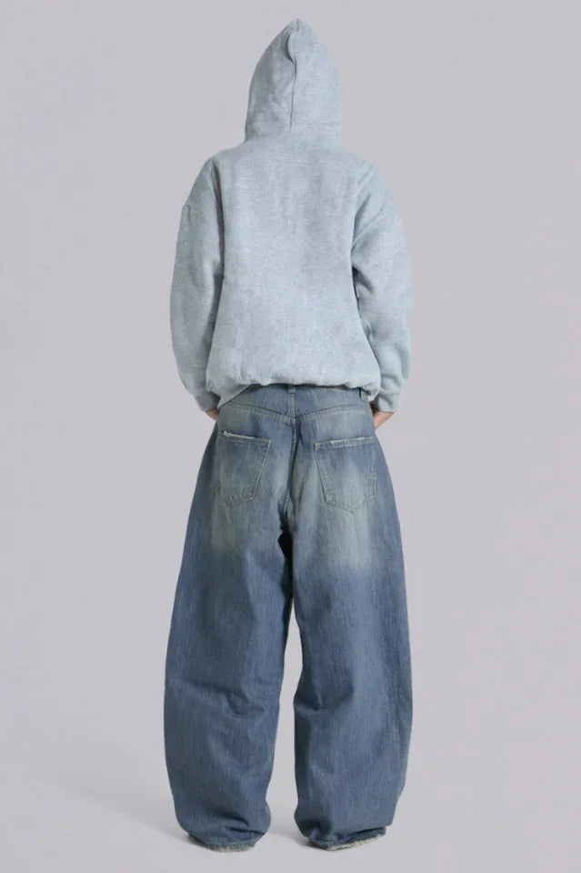Model wearing loose-fitting light wash denim jeans and a light blue zip-up hoodie from the back.