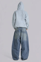Model wearing loose-fitting light wash denim jeans and a light blue zip-up hoodie from the back.