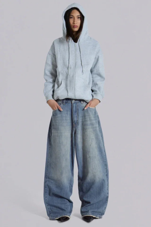 Model wearing loose-fitting light wash denim jeans and a light blue zip-up hoodie from the front.