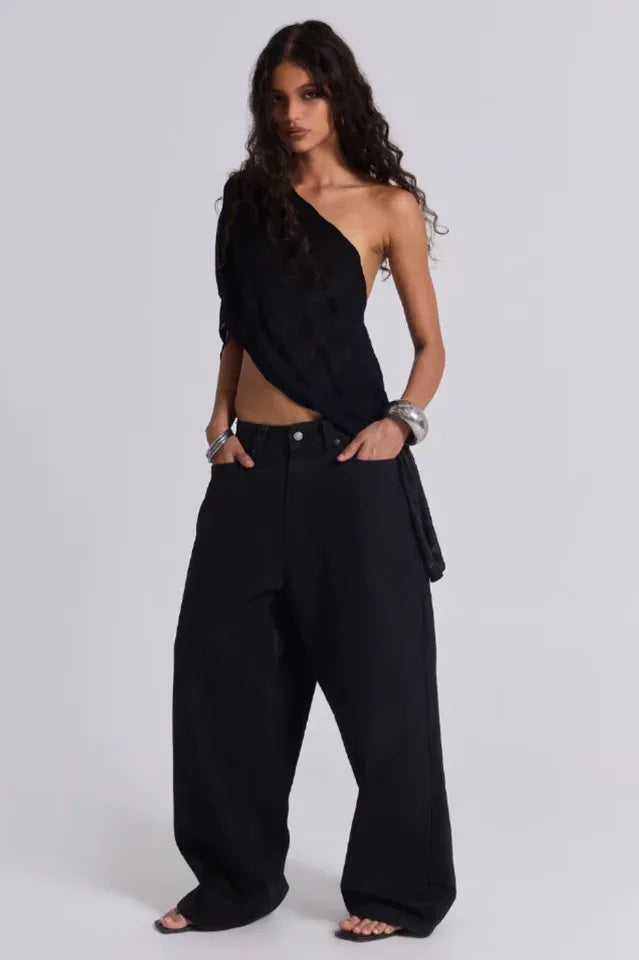 Model wearing wide-leg black pants and a black one-shoulder top with silver bracelets.