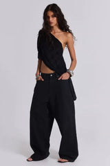 Model wearing wide-leg black pants and a black one-shoulder top with silver bracelets.