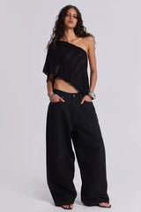 Model wearing wide-leg black pants and a black one-shoulder top with silver bracelets.