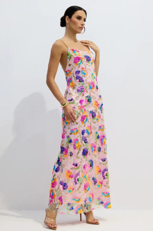 Woman wearing a pink floor-length gown with colorful floral sequins and gold chain straps, standing against a white background.